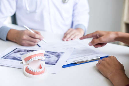 Male doctor or dentist writing report working with tooth x-ray film model and equipment used in the treatment of dental and dentistry and recommend patient at workplace.の写真素材