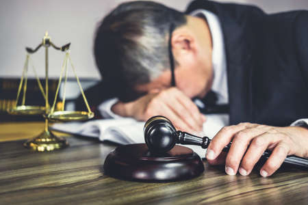 Judge gavel with lawyers, Gavel on wooden table and Counselor or Male lawyer is tired and migraine headaches during hard working on a documents at law firm. Legal law, advice and justice concept.の写真素材