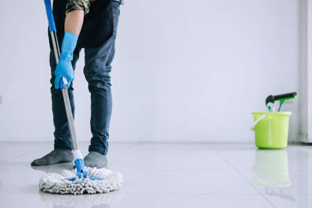 Husband housekeeping and cleaning concept, Happy young man in blue rubber gloves wiping dust using mop while cleaning on floor at home.の写真素材