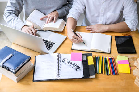 Education, teaching, learning, technology and people concept. Two high school students or classmates with helps friend do homeworks learning in classroom, Tutor books with friends.の写真素材