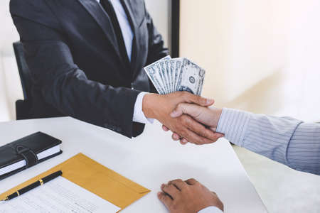 Bribery and corruption concept, bribe in the form of dollar bills, Businessman shaking hands and giving hides money while making deal to agreement a contract.の写真素材