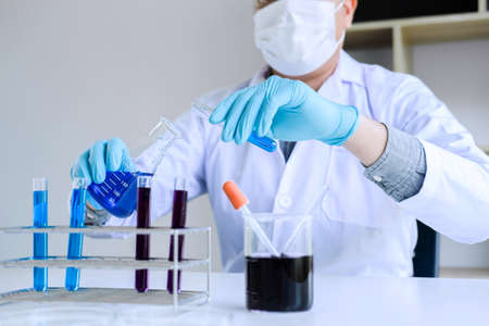 Biochemistry laboratory research, Scientist or medical in lab coat holding test tube with reagent with drop of color liquid over glass equipment working at the laboratory.の写真素材