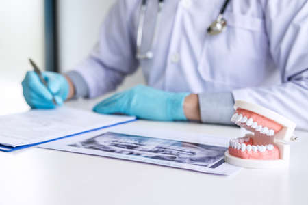Male doctor or dentist working with patient tooth x-ray film, model and equipment used in the treatment and analysis teeth disease of dental and dentistry at workplace.の写真素材
