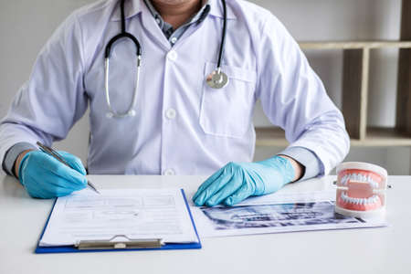 Male doctor or dentist working with patient tooth x-ray film, model and equipment used in the treatment and analysis teeth disease of dental and dentistry at workplace.の写真素材