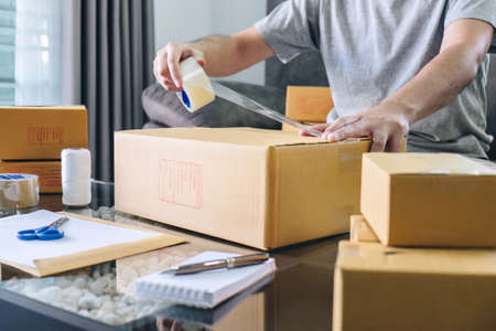 Small business parcel for shipment to client, Young entrepreneur SME freelance man working with packaging their packages box delivery online market on purchase order and preparing package product.の写真素材