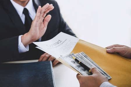 Bribery and corruption concept, senior businessman manager refusing receive money in the envelope to agreement contract, A bribe in the form of dollar bills.の写真素材