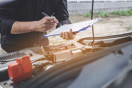 Services car engine machine concept, Automobile mechanic repairman checking a car engine with inspecting writing to the clipboard the checklist for repair machine, car service and maintenance.の写真素材