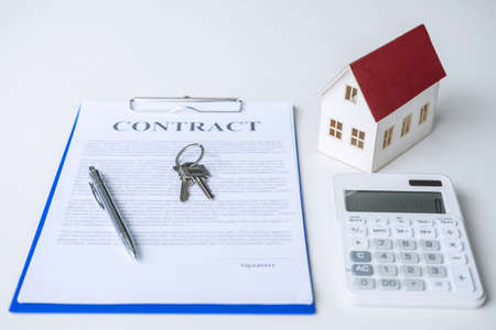 House model, calculator and house key lying on real estate contract, home loan and investment concept.の写真素材