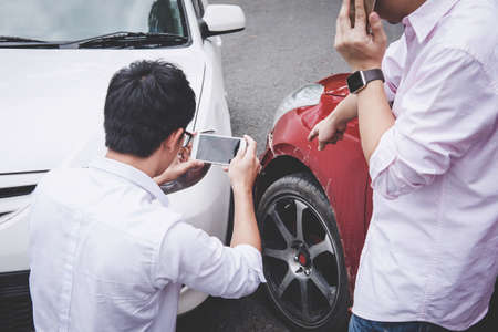 Two drivers man arguing after a car traffic accident collision and making phone call to Insurance Agent and take a photo, Traffic Accident and insurance concept.の写真素材