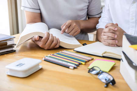 High school tutor or college student group sitting at desk in library studying and reading, doing...