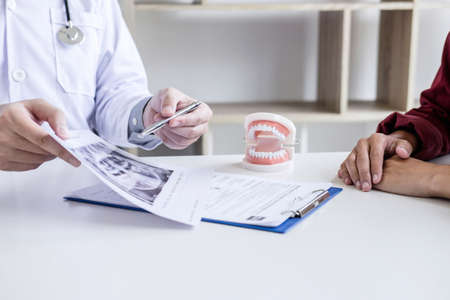Male doctor or dentist writing report working with tooth x-ray film model and equipment used in the treatment of dental and dentistry and recommend patient at workplace.の写真素材