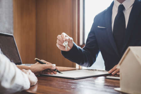 Sales manager filing keys to customer after signing rental lease contract of sale purchase agreement, concerning mortgage loan offer for and house insurance.の写真素材