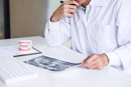 Male doctor or dentist working with patient tooth x-ray film, model and equipment used in the treatment and analysis teeth disease of dental and dentistry at workplace.の写真素材
