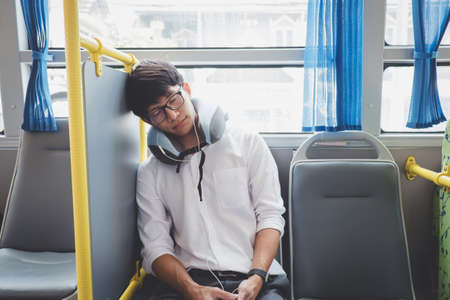 Young Asian man traveler sitting on a bus and sleeping with pillow, transport, tourism and road trip concept.の写真素材