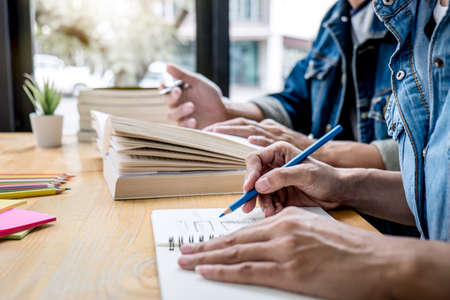 High school tutor or college student group sitting at desk in library studying and reading, doing...