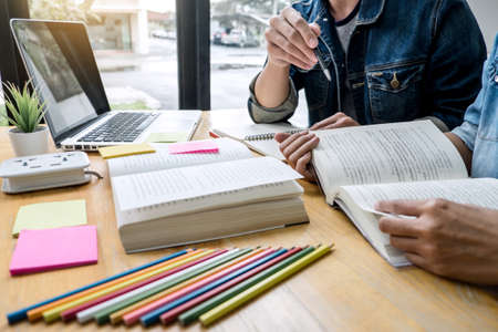 Education, teaching, learning, technology and people concept. Two high school students or classmates with helps friend do homeworks learning in classroom, Tutor books with friends.の写真素材