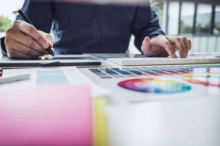 Image of male creative graphic designer working on color selection and drawing on graphics tablet at workplace with work tools and accessories.の写真素材