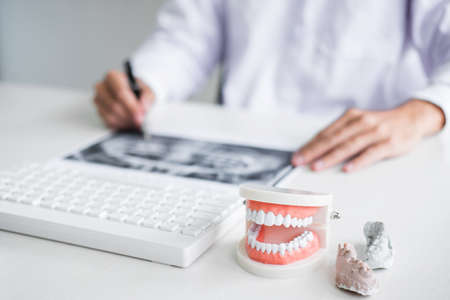 Male doctor or dentist working with patient tooth x-ray film, model and equipment used in the treatment and analysis teeth disease of dental and dentistry at workplace.の写真素材