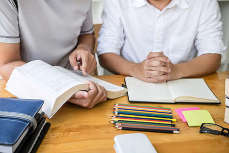 Education, teaching, learning, technology and people concept. Two high school students or classmates with helps friend do homeworks learning in classroom, Tutor books with friends.の写真素材