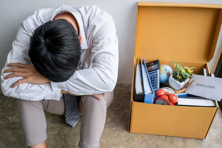 Images of packing up all his personal belongings and files into a brown cardboard box, Businessman has frustrated and stressed to resignation and signing cancellation contract letter in office.の写真素材