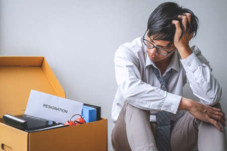 Images of packing up all his personal belongings and files into a brown cardboard box, Businessman has frustrated and stressed to resignation and signing cancellation contract letter in office.の写真素材