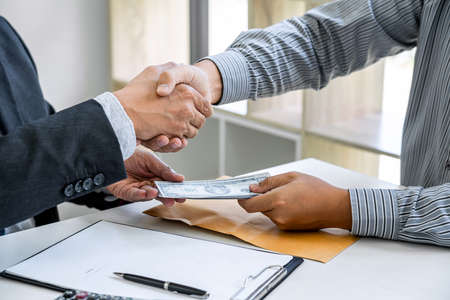 Bribery and corruption concept, bribe in the form of dollar bills, Businessman shaking hands and...