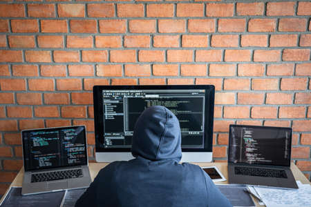 Computer hacker or cyber attack concept, Dangerous hooded hacker using multiple computers typing bad data into online system the access with a virus to infect steal information.の写真素材