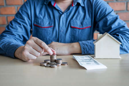 Man putting coins into money box with savings and analysis business investment strategy home loan with income of money coin and dollar for future real estate.の写真素材
