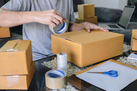 Small business parcel for shipment to client, Young entrepreneur SME freelance man working with packaging their packages box delivery online market on purchase order and preparing package product.の写真素材