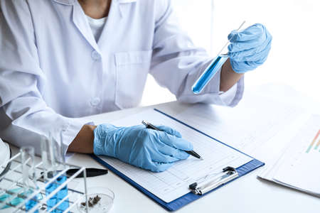 Scientist or medical in lab coat holding test tube with reagent, Laboratory glassware containing...