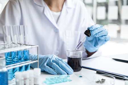 Scientist or medical in lab coat holding dropper with reagent, mixing reagents in glass flask, glassware containing chemical liquid, laboratory research and testing of Microscope.の写真素材