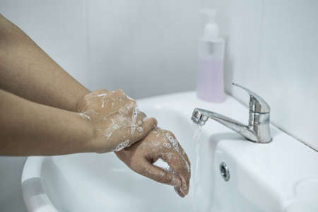 Woman washing hands under the water tap in bathroom with using soap gel for cleaning and prevention...