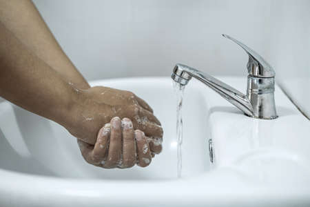 Woman washing hands under the water tap in bathroom with using soap gel for cleaning and prevention inflection coronavirus.の写真素材
