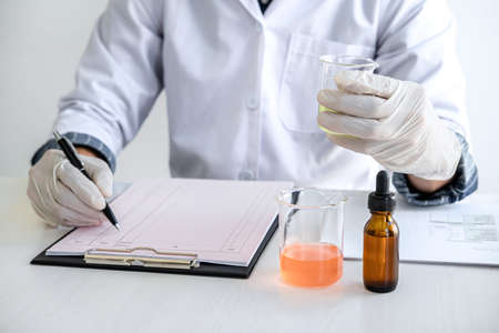 Scientist or medical in lab coat holding test tube with reagent, mixing reagents in glass flask,...