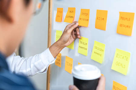 Two creative Business people meeting and planning use post it notes sticky note on board to share idea, Analysis data charts and graph with teamwork strategy brainstorming.の写真素材