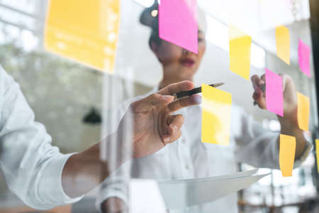 Young creative team professional using post it notes in glass wall to writing strategy business plan to development grow to success.の写真素材
