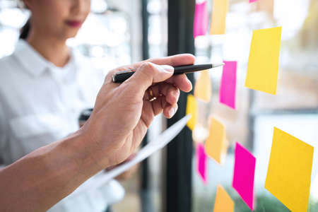 Young creative team professional using notes in glass wall to writing strategy business plan to...