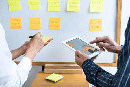 Two creative Business people meeting and planning use post it notes sticky note on board to share...