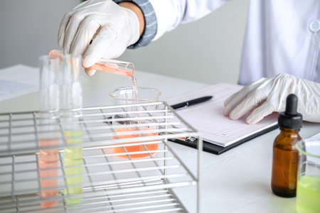 Scientist or medical in lab coat holding test tube with reagent, mixing reagents in glass flask, glassware containing chemical liquid, laboratory research and testing.の写真素材