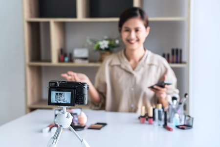 Happy smiling elegant woman or beauty blogger with brush on recording video while review product make up tutorial for theme about video blogging on camera screen.の写真素材