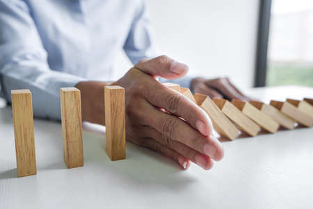 Risk and strategy in business, Close up of business woman hand stopping wooden block between three way from falling in the line of domino.の写真素材