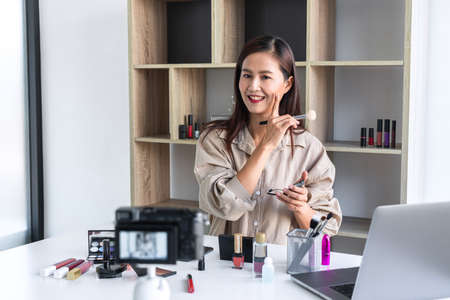 Happy smiling elegant woman or beauty blogger with brush on recording video while review product make up tutorial for theme about video blogging on camera screen.の写真素材