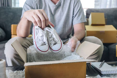 Small business parcel for shipment to client, Young entrepreneur SME freelance man working with packaging shoe into box delivery online market on purchase order and preparing package product at home.の写真素材