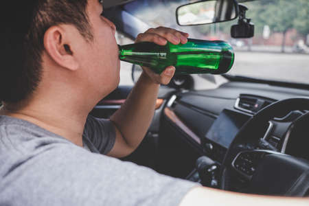 Young asian man drives a car with drunk a bottle of beer behind the wheel of a car.の写真素材