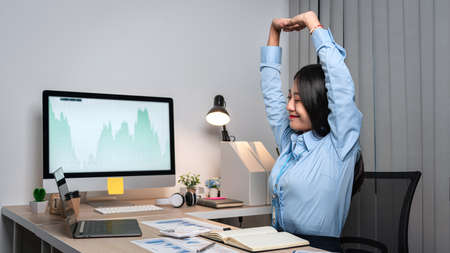 Young Asian Business woman sitting on the chair stretching herself and exercise for relaxation while working hard at office.の写真素材