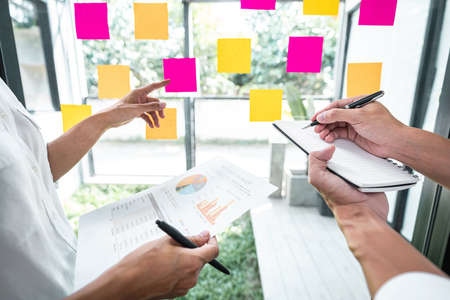 Young creative team professional using sticky notes in glass wall to writing strategy business plan...