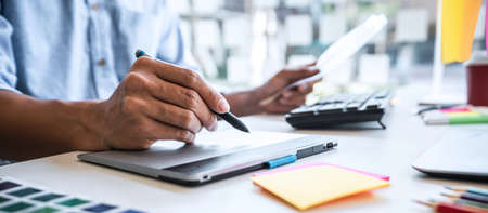 Image of male creative graphic designer working on color selection and drawing on graphics tablet at workplace with work tools and accessories in workspace.の写真素材