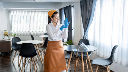 Asian woman waitress wearing glove and face shield to prevent and stop coronavirus before working...