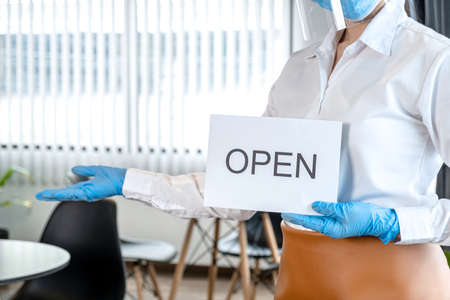 Close up of asian woman waitress wearing protective face mask and medical glove to holding open sign...