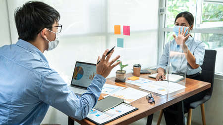Two business colleagues wearing face mask to brainstorming business project and giving high five to...